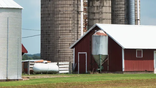 industrial-propane-tanks a close up photo of a propane tank on a farm between a barn and a couple silos